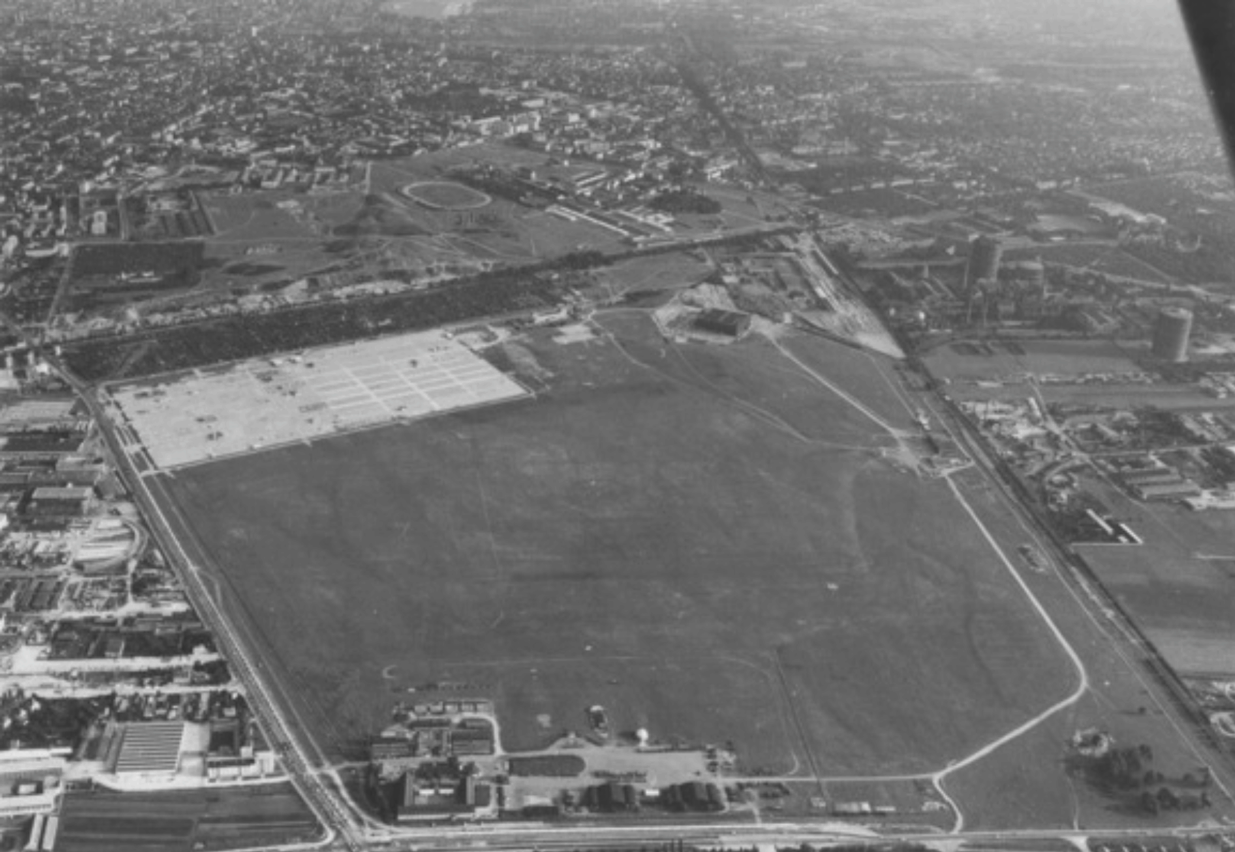 1963: Blick in Richtung Süden, unbebautes Oberwiesenfeld, im unteren Bildschirmbereich die alten Abfertigungshallen|600